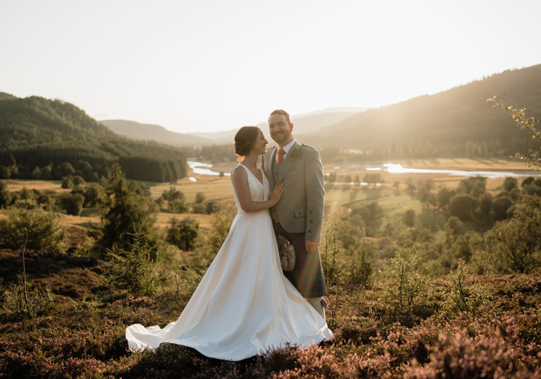 bride and groom standing in the heather with the Linn of Dee and Mar Lodge in the background 